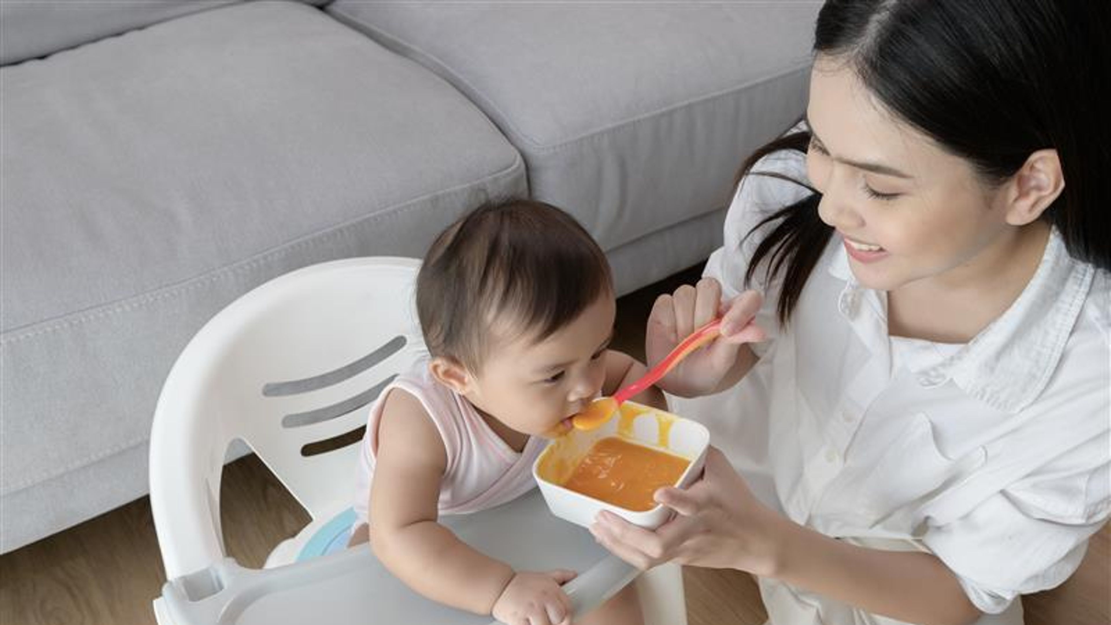 Mother helping baby eating blend food on baby chair