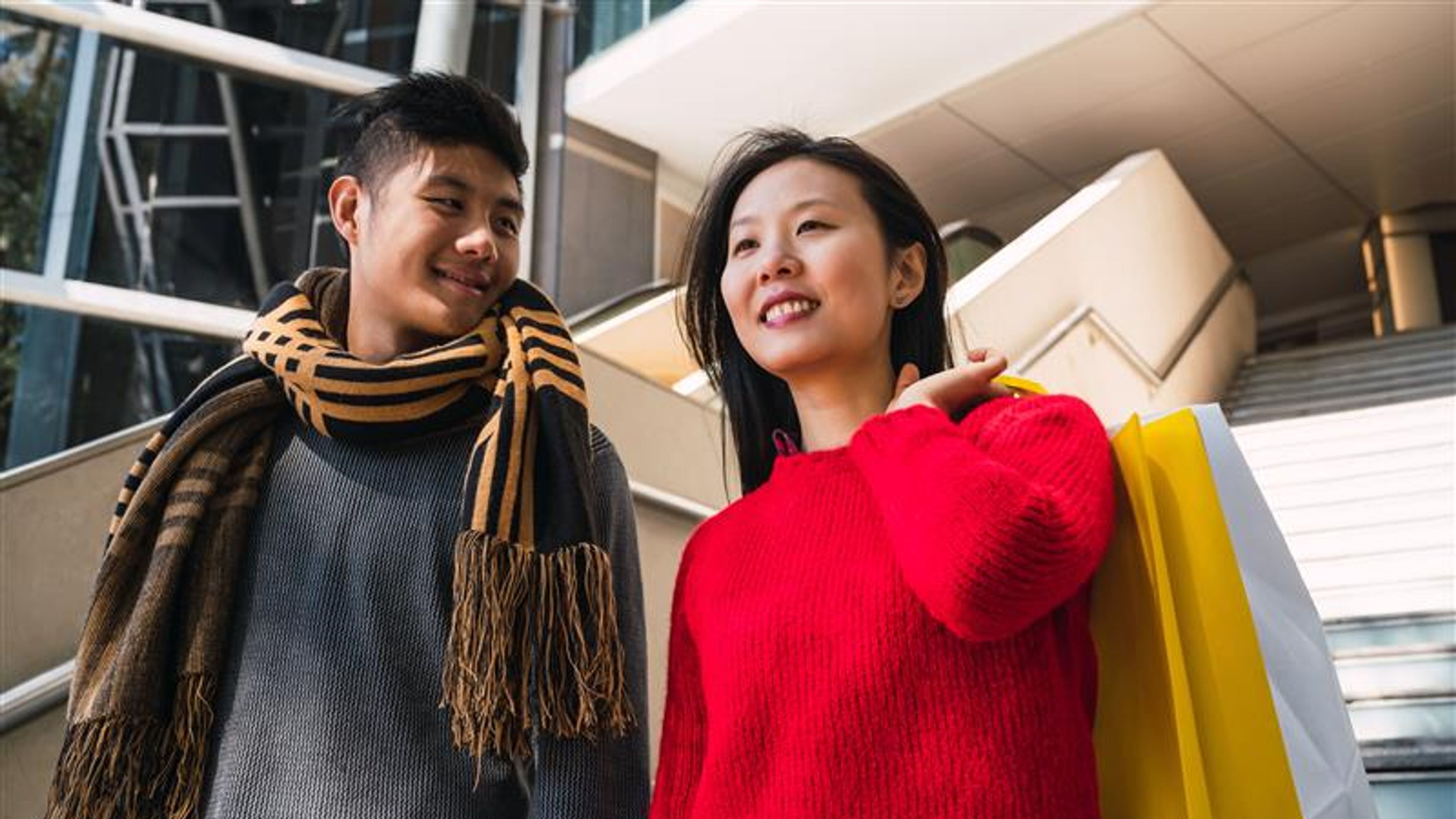 Portrait of lovely Asian couple holding colorful shopping bags and enjoying shopping