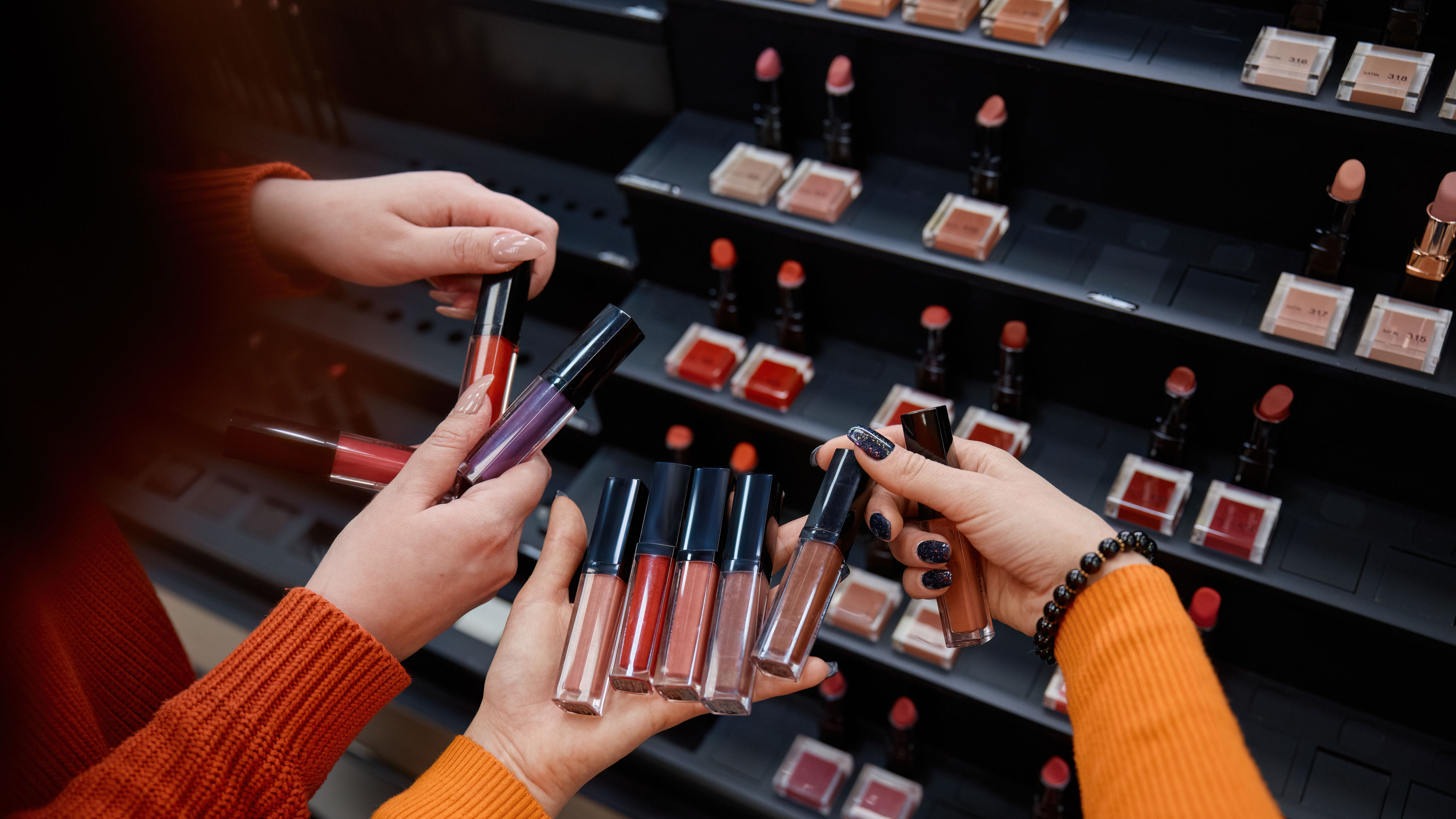 Three people are holding several lip glosses in different shades.