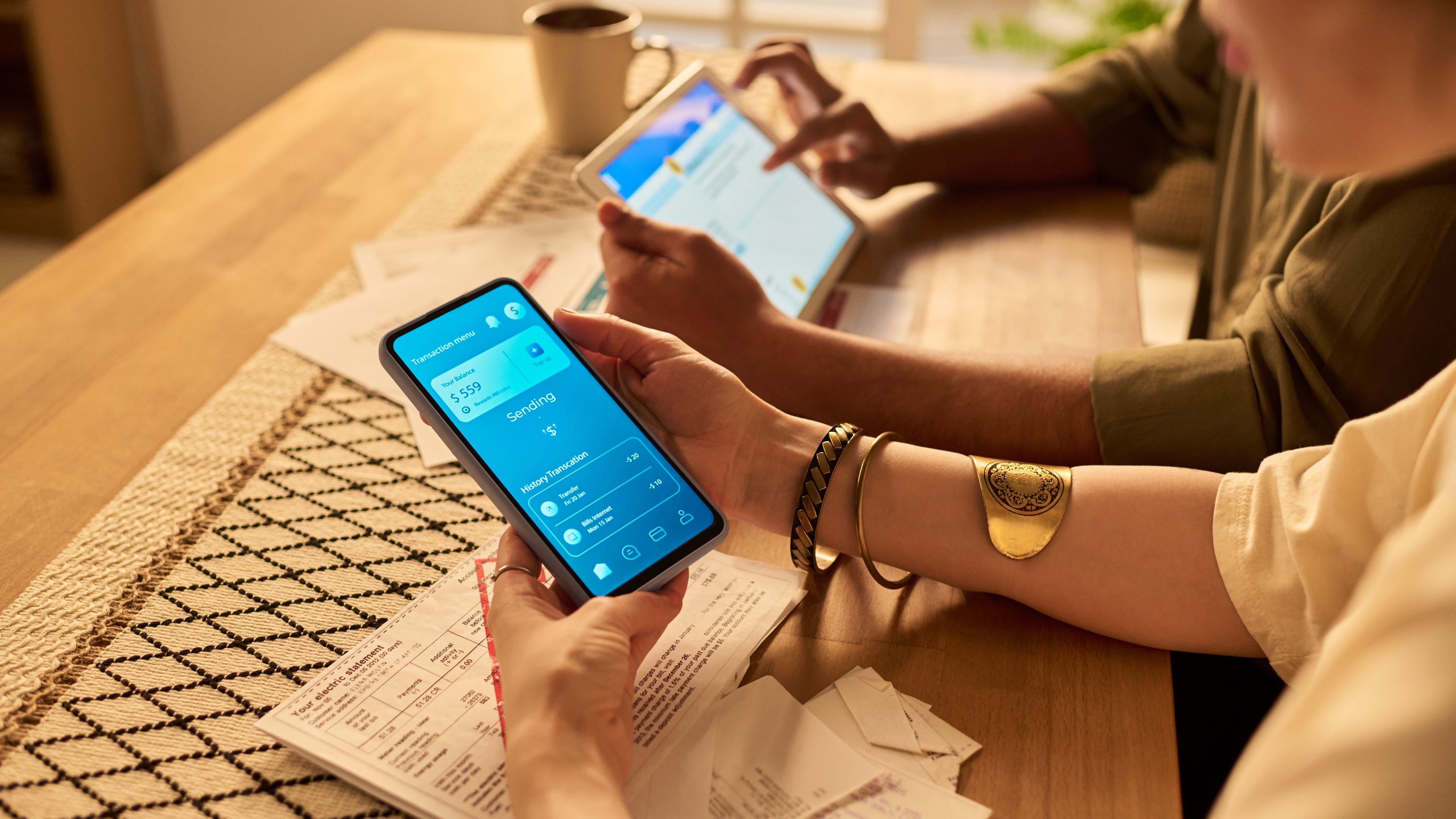 Two people sitting at a wooden table using smartphones and tablets for financial management