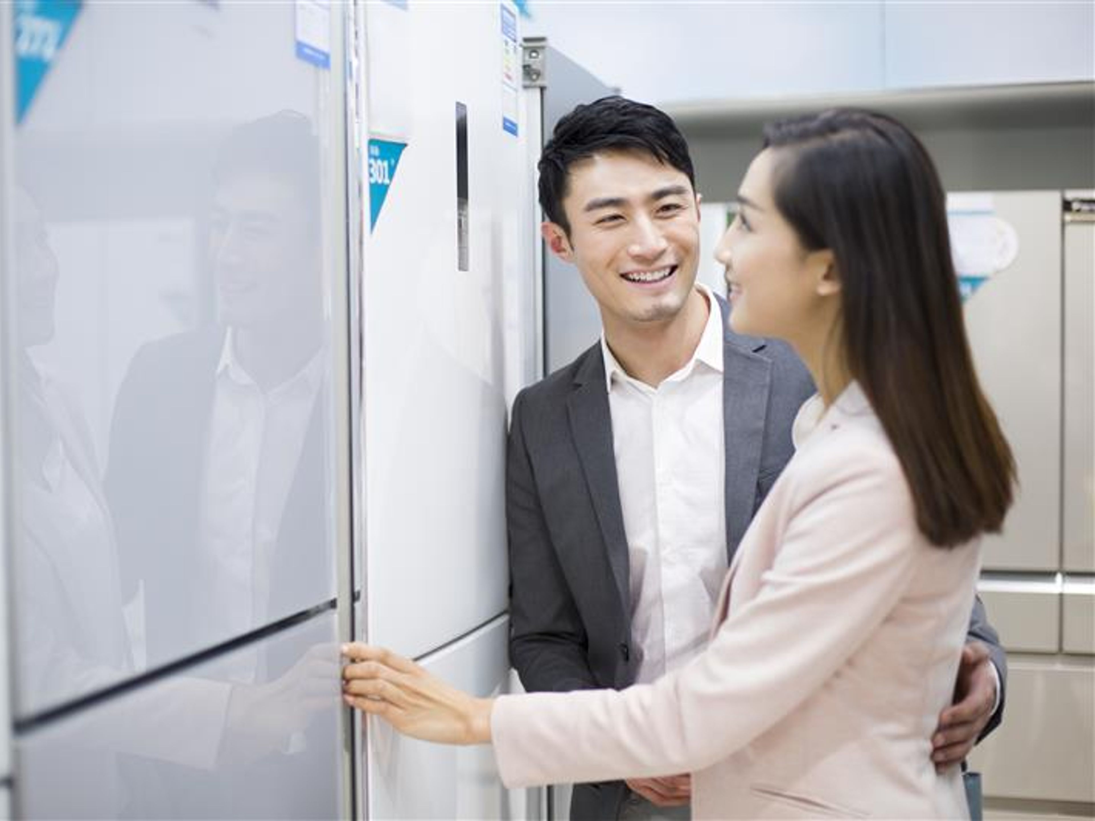Two people smiling and looking at the refrigerator.