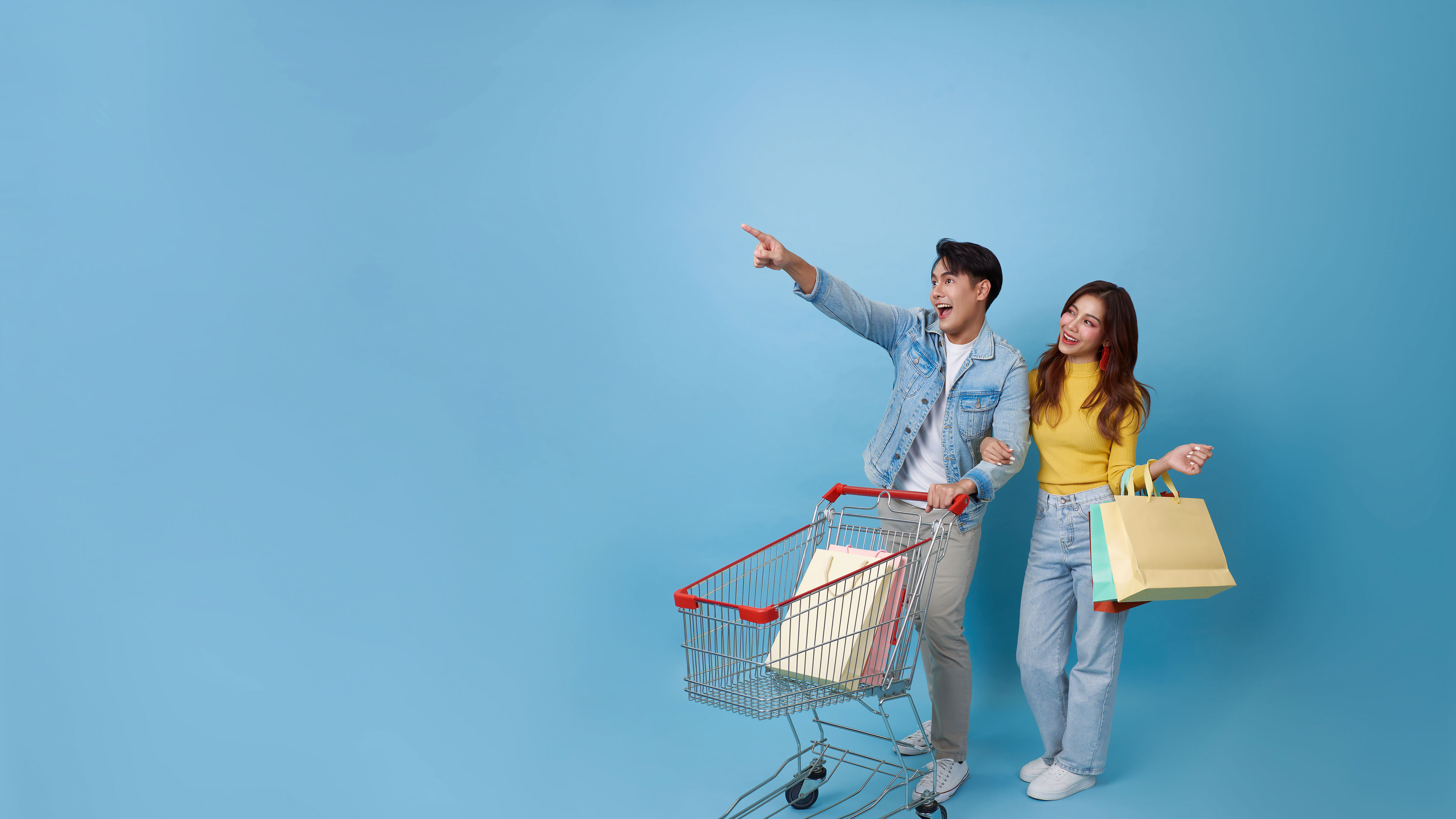 Young cheerful Asian couple have fun with shopping trolley cart and holding shopping bag.