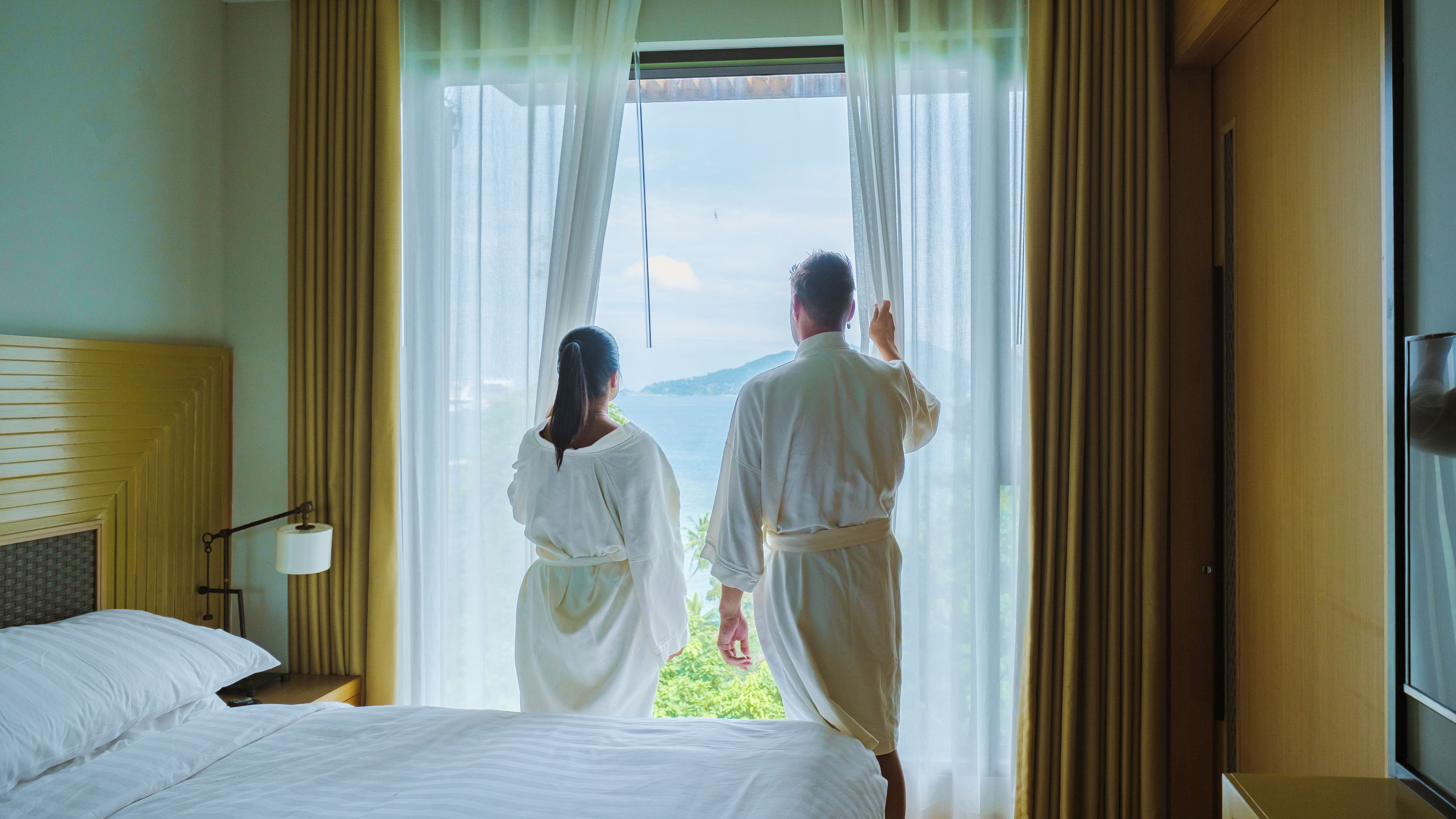 Men and women waking up in a hotel room looking out over the ocean.