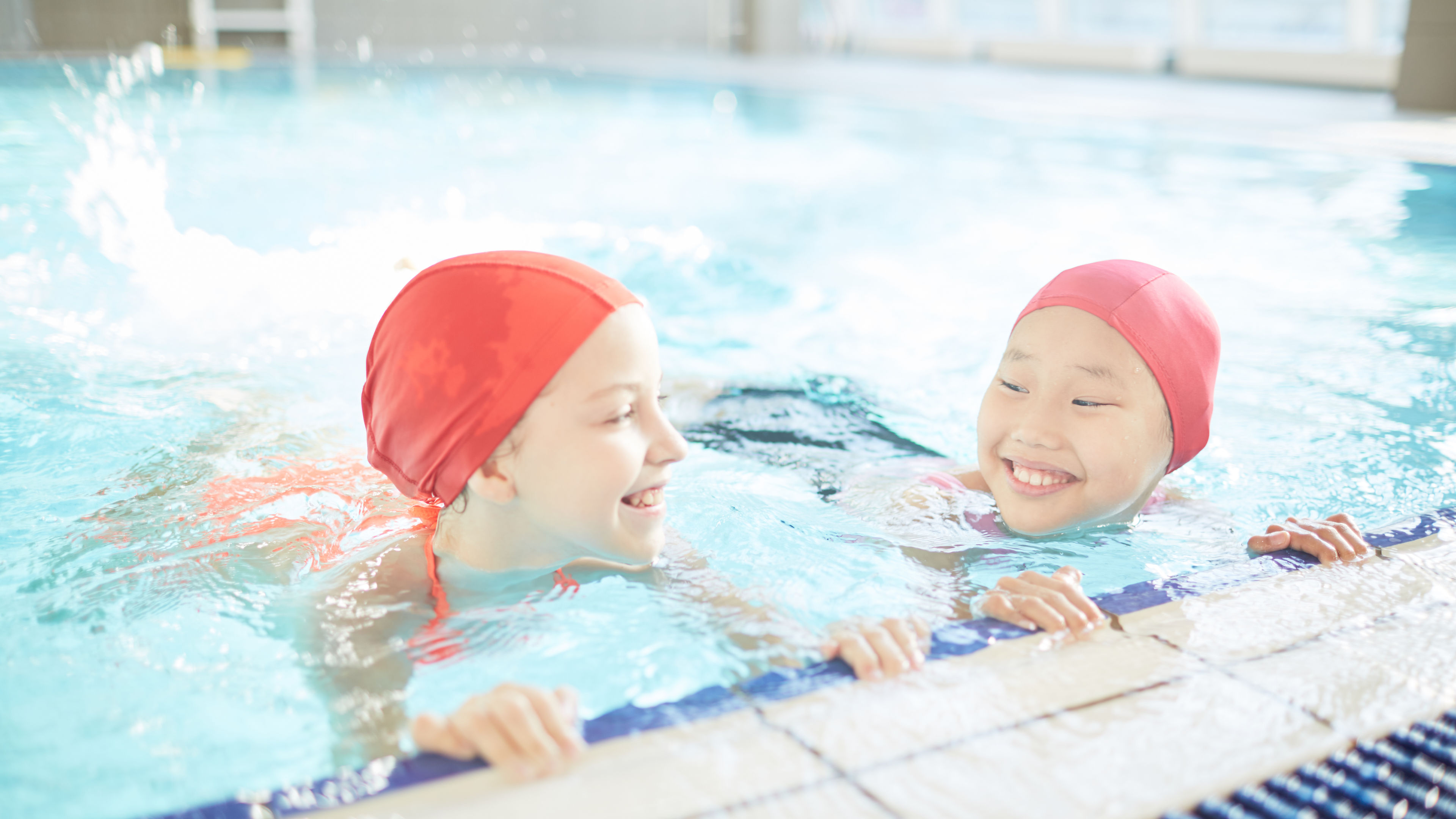 Two friendly girls having fun while practicing swimming in pool